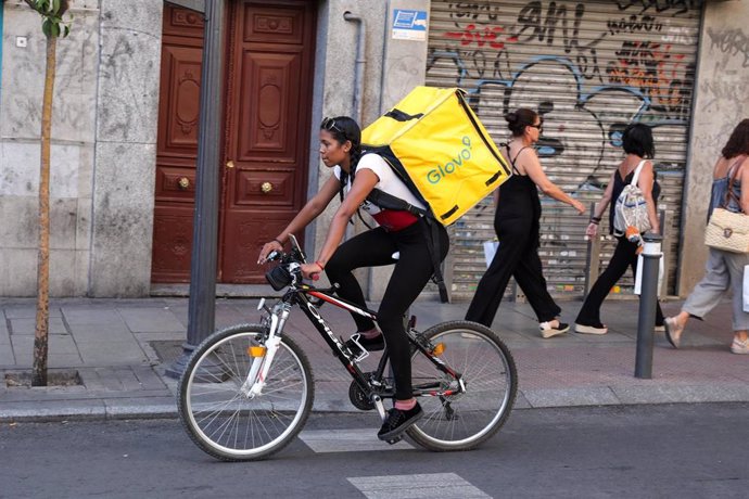 Fotografía de una repartidora  de la empresa Glovo transitando en bicicleta por una calle del centro de Madrid.