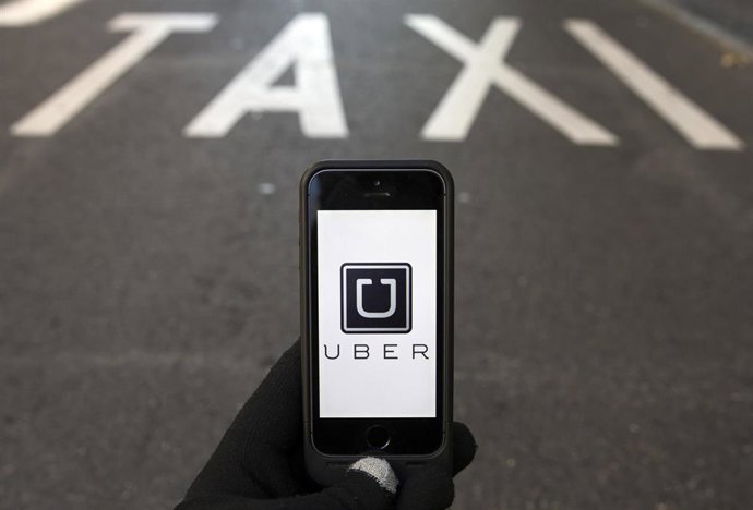 Photo illustration of logo of car-sharing service app Uber on a smartphone over a reserved lane for taxis in a street in Madrid