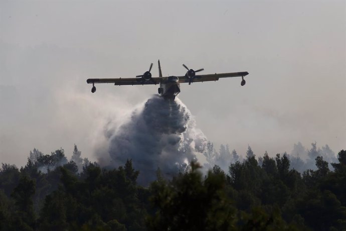 Un avión dscarga agua sobre el bosque en llamas en Eubea
