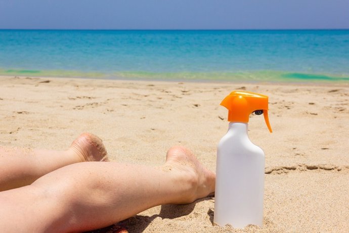 Piernas de mujer boca abajo sobre la arena en la playa, botella de spray de loción solar