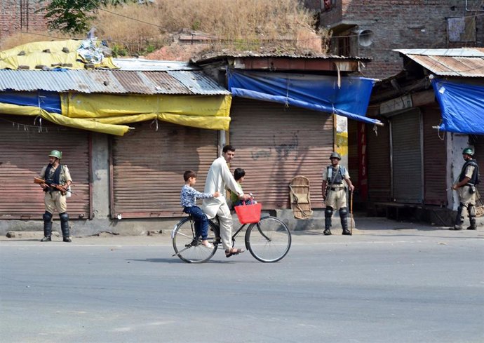 Un hombre pasea en bicicleta frente a miembros de las fuerzas de seguridad en Cachemira