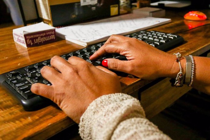 Unes mans de dona escriuen en el teclat d'un ordinador, sobre una taula de fusta.