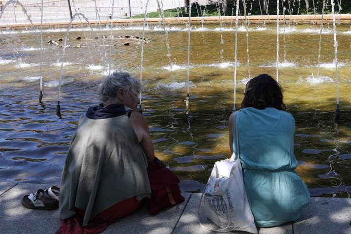 Dos mujeres se sientan para refrescarse de las altas temperaturas en una fuente