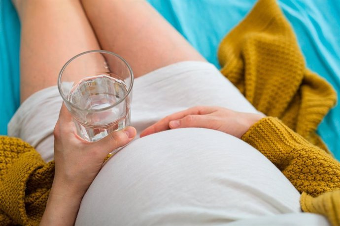 Embarazada sostiene un vaso de agua.