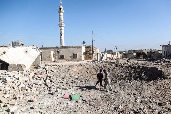Personas junto al cráter dejado por un bombardeo aéreo en Idlib