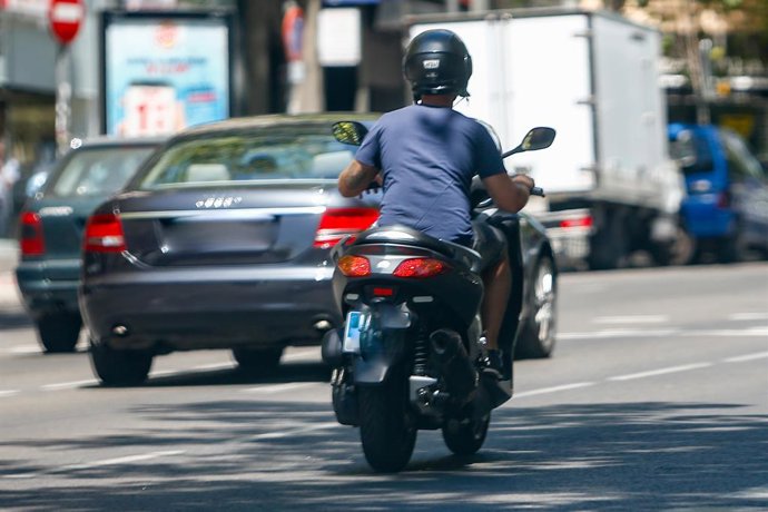 Un home circula en la seva moto per un carrer al costat d'altres vehicles.