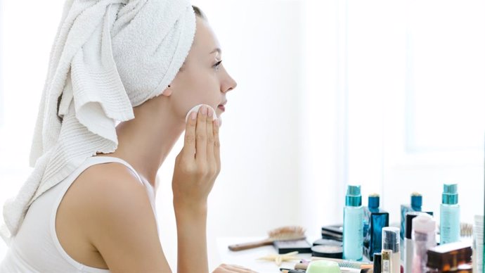 Mujer retirándose el maquillaje y dándose crema ante el espejo.