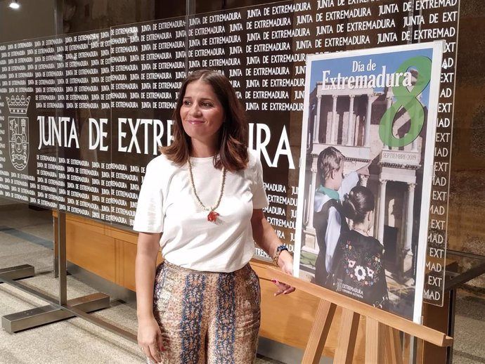 Isabel Gil Rosiña, posa junto al cartel del Día de Extremadura
