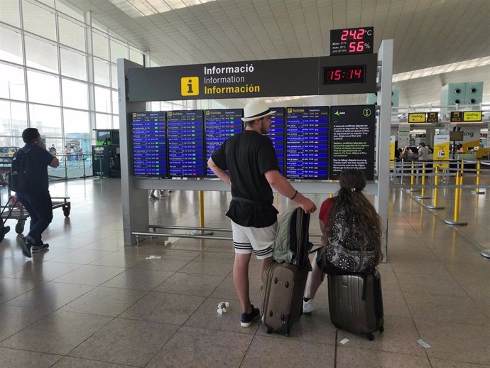 Pasajeros en el Aeropuerto de Barcelona ante un panel de información.