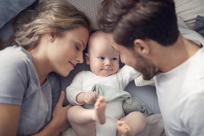 Imagen de una pareja de padres con el bebé en la cama