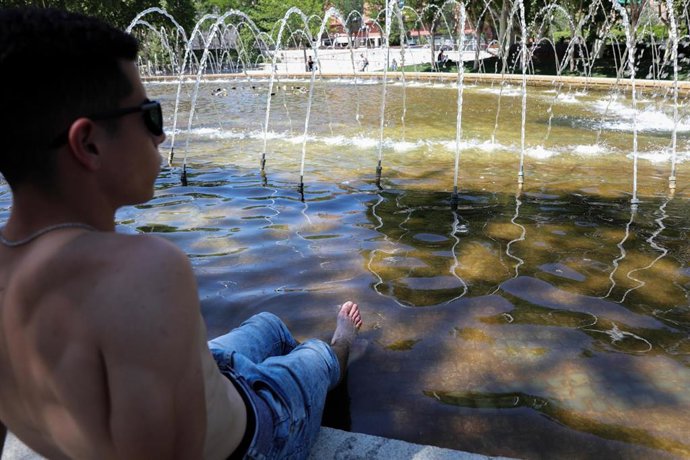 Un joven moja sus piernas para refrescarse de las altas temperaturas en las inmediaciones de los chorros de Madrid Río un día antes de que, según la Agencia Estatal de Meteorología (AEMET), llegue a la península Ibérica y a las Islas Baleares la primera