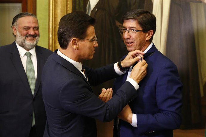 El vicepresidente de la Junta y consejero de Turismo, Regeneración, Justicia y Administración Local, Juan Marín (d), recibe una insignia del alcalde de la capital, Luis Salvador (c) durante su visita, En el Consistorio.