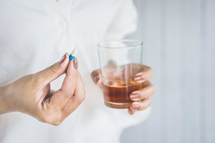 Mujer  tomando medicamentos con un vaso de alcohol