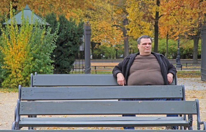 Fat man is sitting on a bench in park of