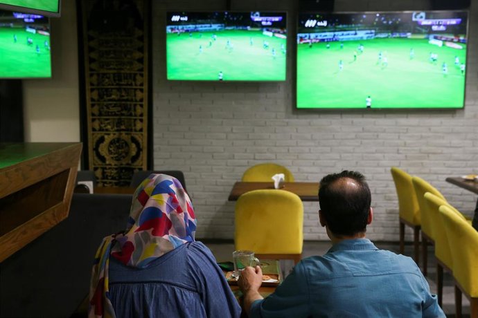 Una mujer ve un partido de fútbol junto a un amigo en una cafetería de Irán
