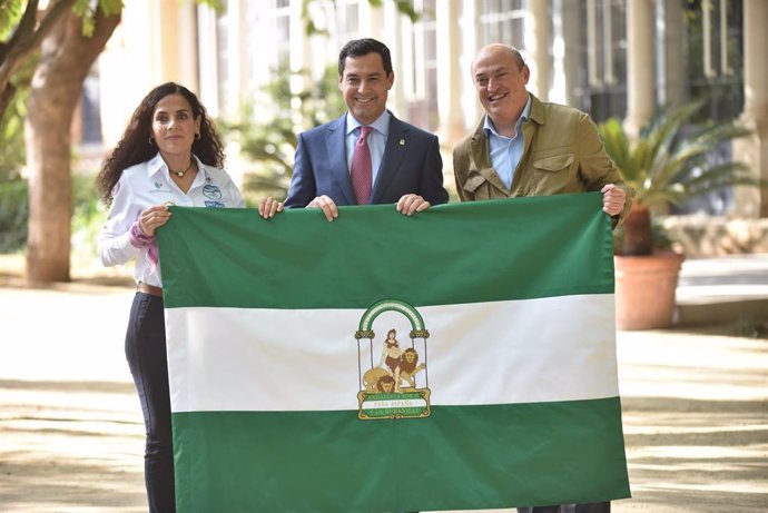 El presidente de la Junta, Juanma Moreno, entrega una bandera de Andalucía a Felisa Requena y Eric Frattini, participante y creador del Reto Pelayo Vida.