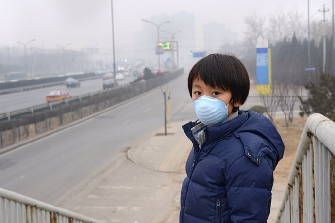 Muchacho asiático con máscara bucal contra la contaminación del aire (Beijing)