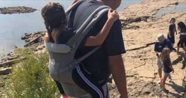 Un profesor lleva a cuestas a una niña con espina bífida para que pueda asistir a una excursión al aire libre