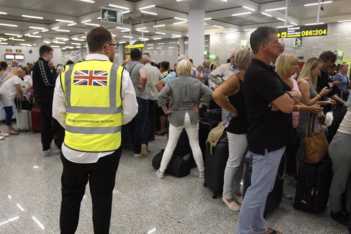 Un guarda de seguridad británcio observa a los turistas que hacen cola frente a los mostradores de la compañía Thomas Cook en el aeropuerto de Palma de Mallorca (Baleares), horas después de que la compañía británica anunciase su quiebra y de que varios 