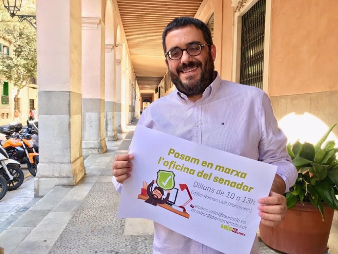 El senador de MÉS per Mallorca,  Vicen Vidal, posa amb un cartell promocional de 'L'oficina del Senador'.