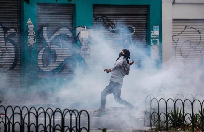07 October 2019, Ecuador, Quito: A masked demonstrator throws stones at security forces during a protest against the increase in fuel prices. The Ecuadorian government has declared a state of emergency for 60 days. Photo: Juan Diego Montenegro/dpa