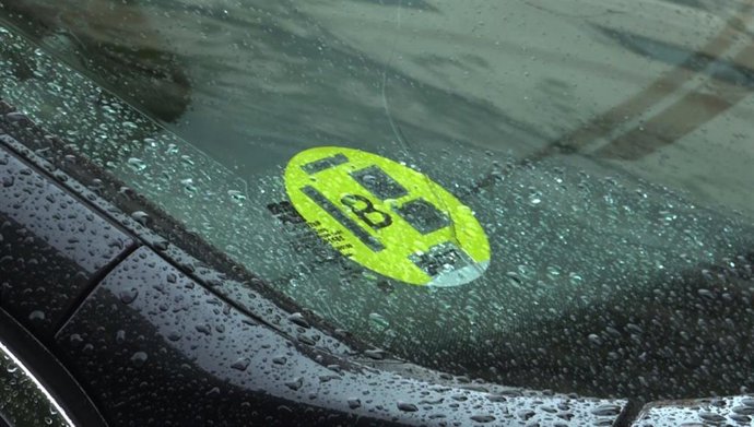 Un coche con un distintivo ambiental de la Dirección General de Tráfico (DGT) de  tipo B, pegado en la luna.  