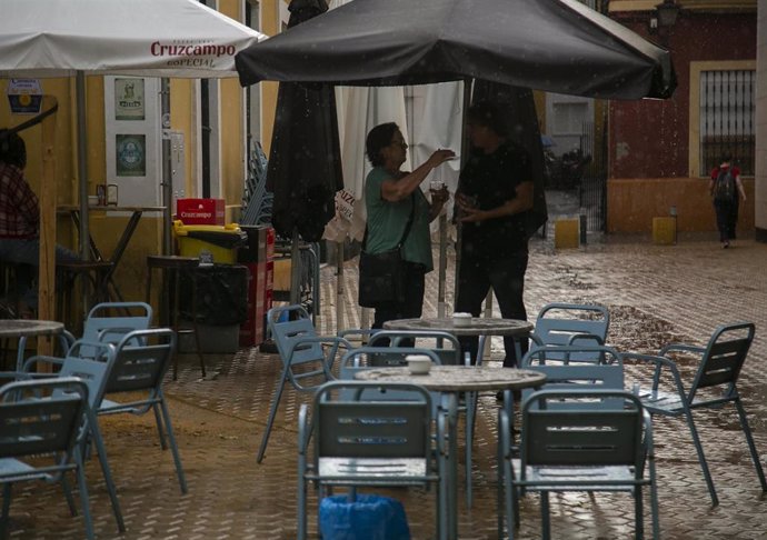 Clientes de un bar se refugian de la lluvia bajo la sombrilla