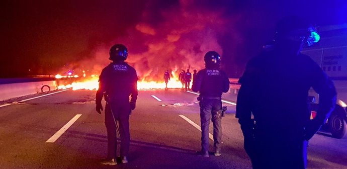 Mossos davant d'una barricada cremant a l'autovia AP7 prop de Girona per la vaga general a Catalunya.