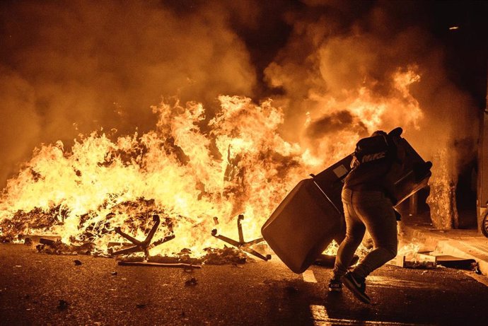 15 October 2019, Spain, Barcelona: A pro-independence protester carries an object past a burning barricade during clashes that erupted after Spain's supreme court sentenced nine Catalonian separatist leaders to between nine and 13 years in prison over t