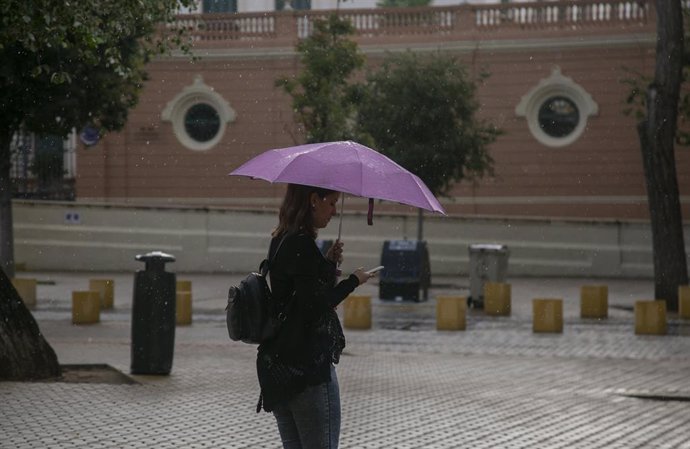 Una mujer se protege de la lluvia bajo su paragüas mientras camina. Sevilla.