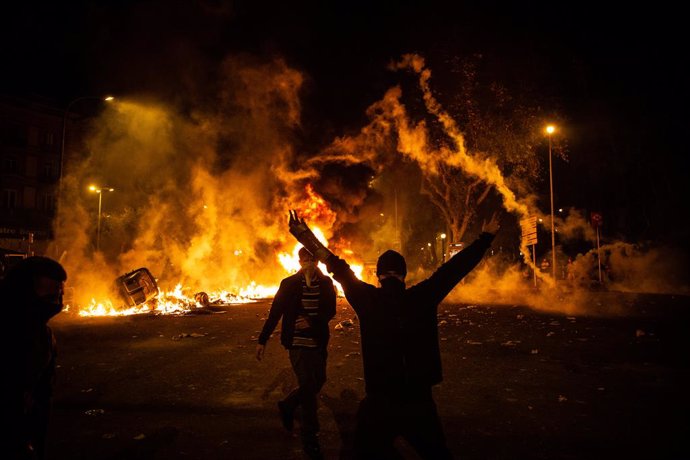 Un manifestant aixeca els braos al costat del foc d'una foguera durant els disturbis a la Plaa d'Urquinaona.