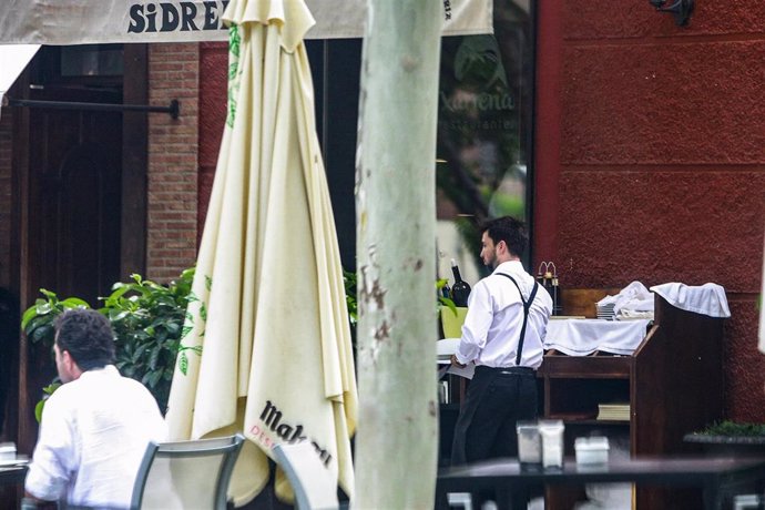 Un camarero atiende a las mesas de en una terraza de una sidrería.