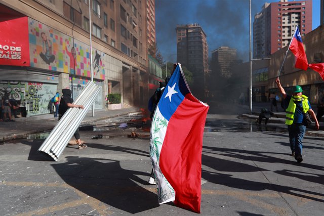 dpatop - 24 October 2019, Chile, Santiago: People hold Chilean flag during clashes with police, following a protest against government, at Plaza Baquedano formerly known as Plaza Italia. Photo: Francisco Estrada/NOTIMEX/dpa