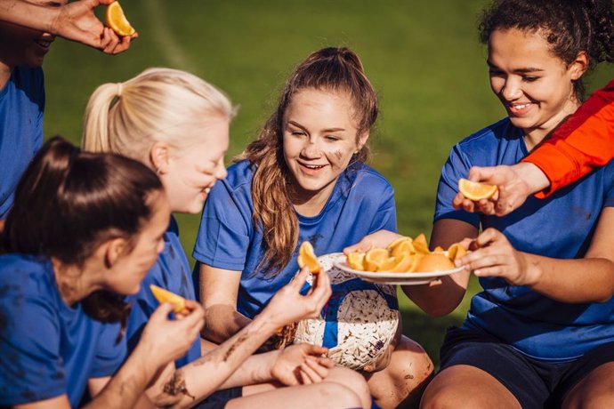 Adolescentes futbolistas femeninas tomando una naranja para reponer fuerzas.