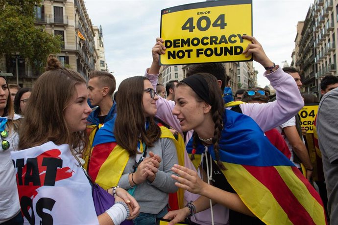Un chico sujeta un cartel en el que se lee, `Error 404 Democrazy Not Found junto a otras chicas con la bandera de la estelada 