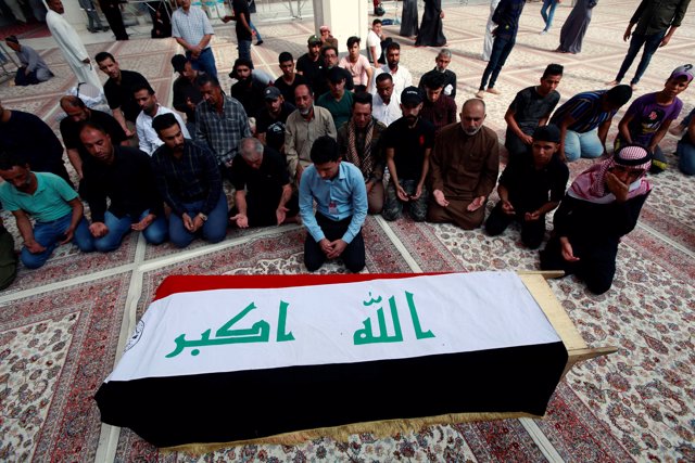 Iraqi men mourn over the coffin of a demonstrator