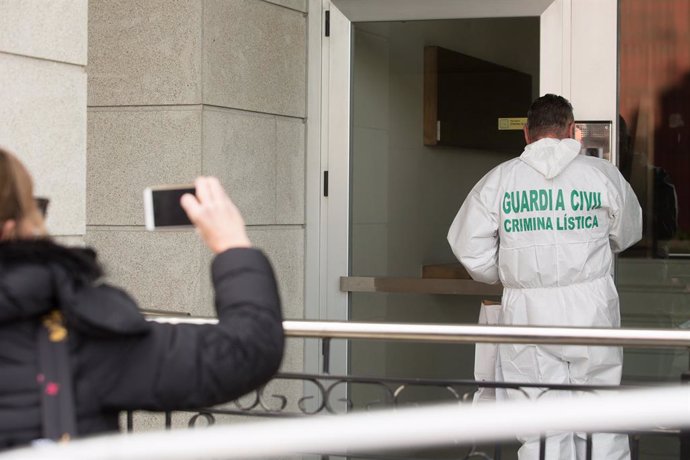 Una dona fotografia un treballador de Criminalística de la Gurdia Civil que entra a l'habitatge on un menor d'edat va assassinar presumptament la seva mare la nit de diumenge a dilluns, a Foz (Galícia).