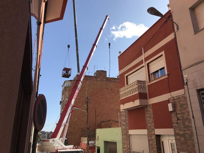 La cesta de una de las grúas con antenas y material del derribo del edificio de Badalona (Barcelona) afectado por aluminosis