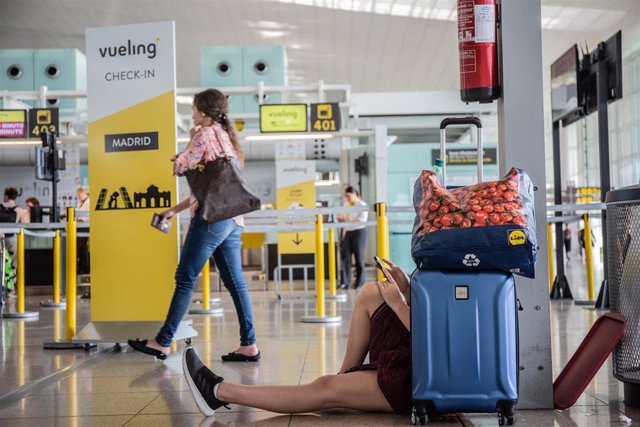 Un joven mira su movil sentado junto a su maleta, junto al puesto de Check-in de la compañía, Vueling en el Aeropuerto 'Josep Tarradellas Barcelona-El Prat', durante la Huelga del personal de tierra de Iberia en Barcelona.