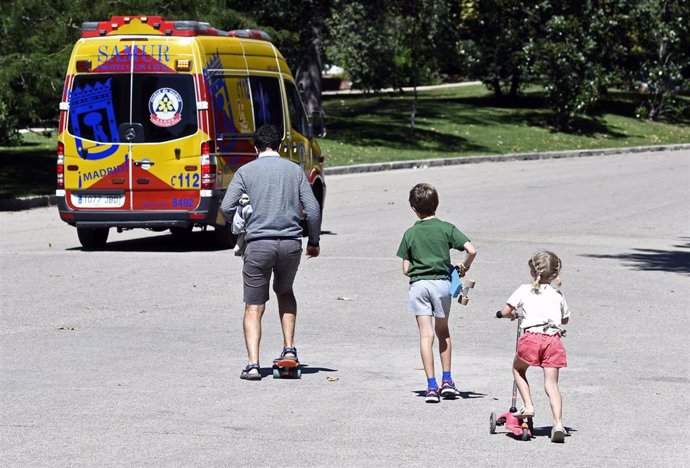 Un padre y sus dos hijos, todos con patinete, en un parque de Madrid.