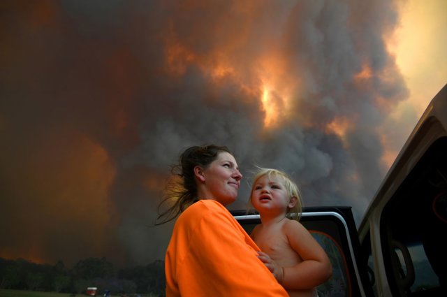 Sharnie Moren and her 18-month-old daughter Charlotte look on as thick smoke rises from bushfires near Nana Glen, near Coffs Harbour, Australia