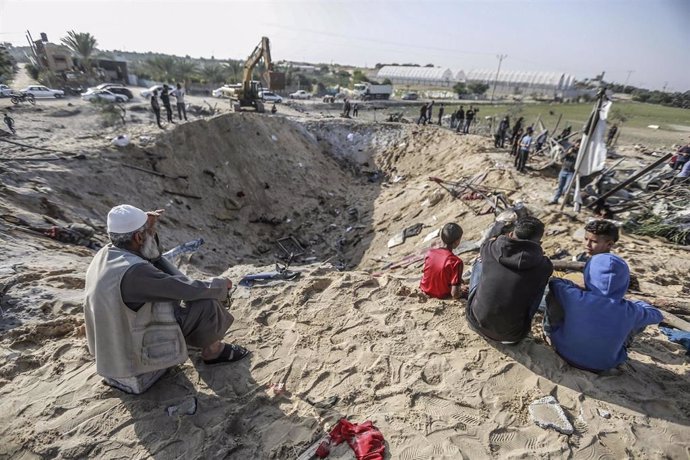 Palestinos sentados en un pedazo de tierra destruido por el impacto de un proyectil israelí