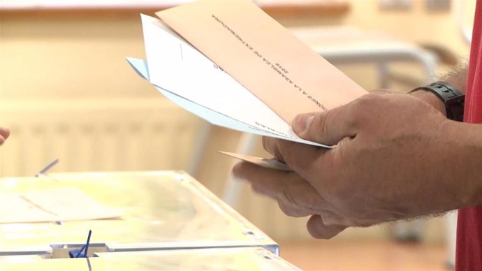 Un elector con las papeletas del 26M junto a una urna.