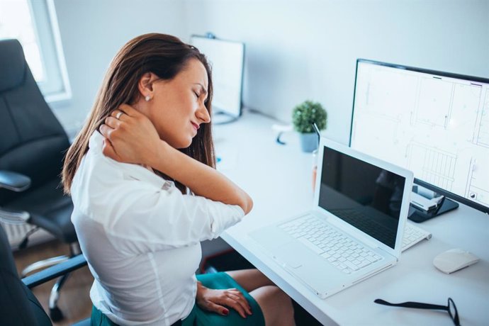 Mujer con dolor en el cuello, contractura, en la oficina trabajando en un ordenador.