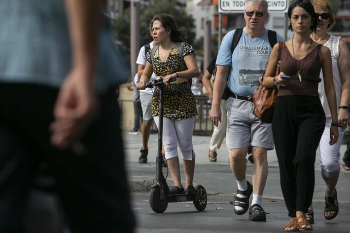Imágenes de recursos de patinetes eléctricos. Una mujer circula por el carril bicil con su patinete eléctrico.
