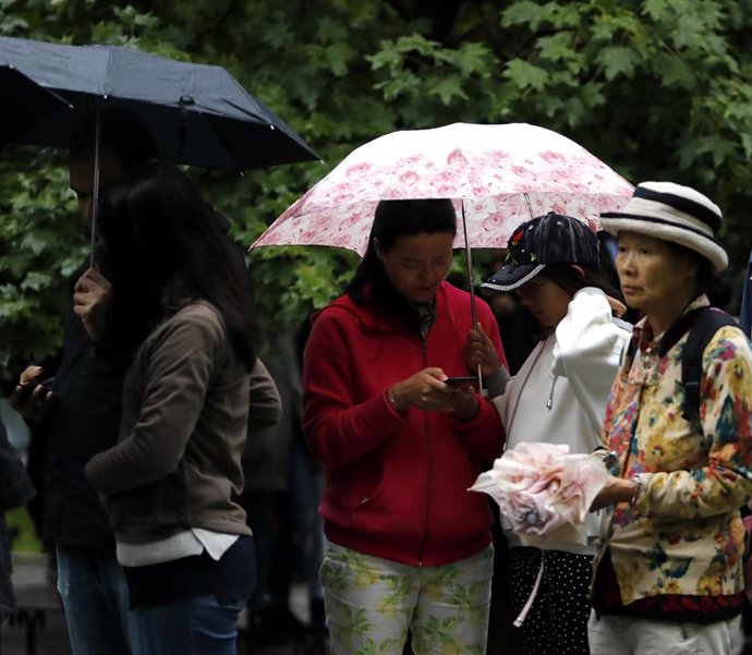 Turistas asiáticos hacen cola con paraguas y bajo la lluvia