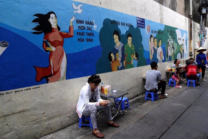 Varias personas comen delante de un mural en la ciudad vietnamita de  Ho Chi Minh.