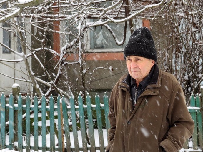 Old man during a snowfall. Cold weather, first snow