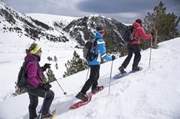 Tres personas suben una montaña con raquetas de nieve