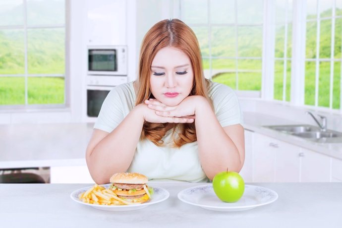 Unhappy woman choosing apple or burger
